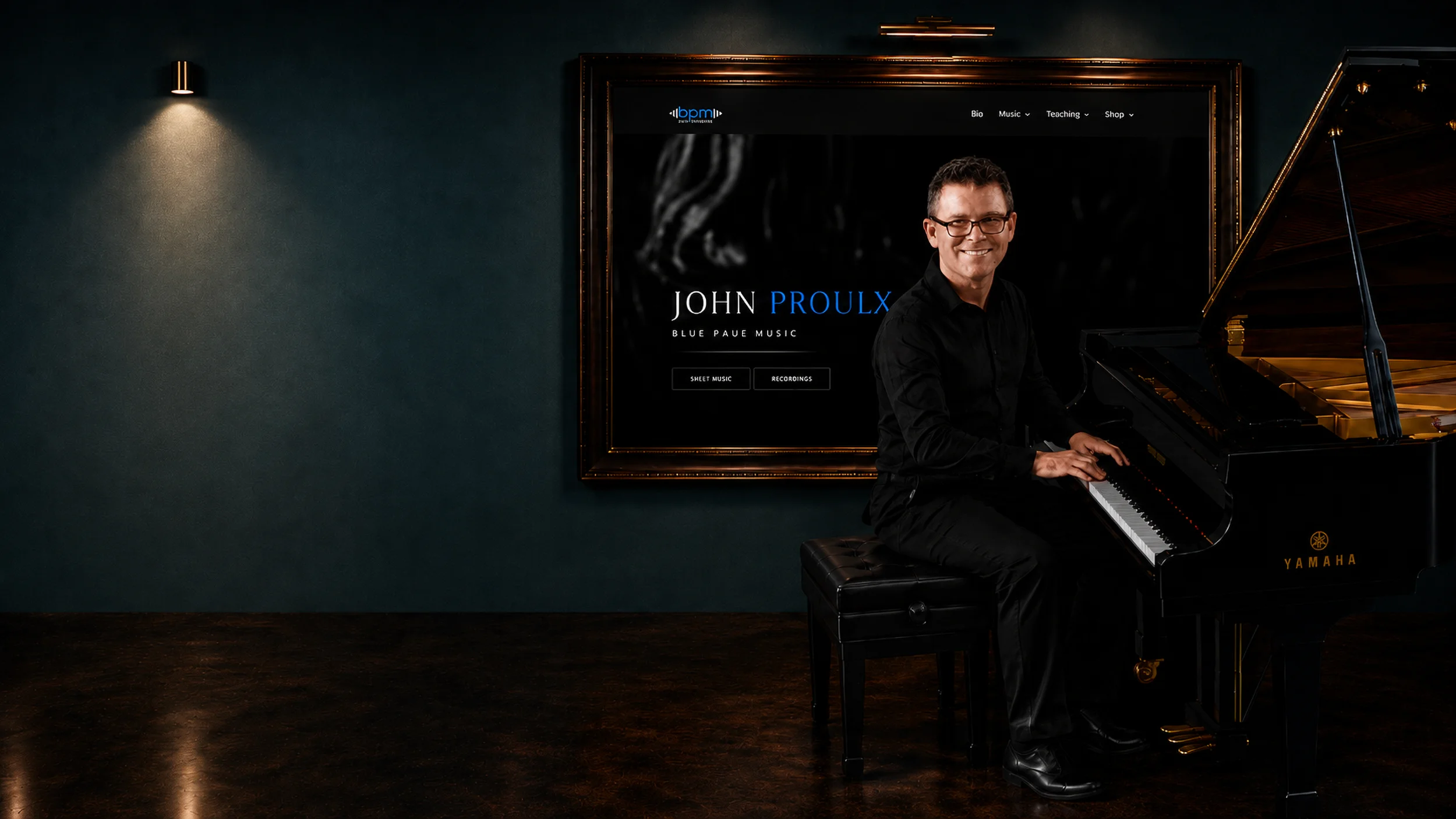 John Proulx - Blue Prue Music: the pianist seated at a grand piano beside his framed site, in a lamplit gallery room.
