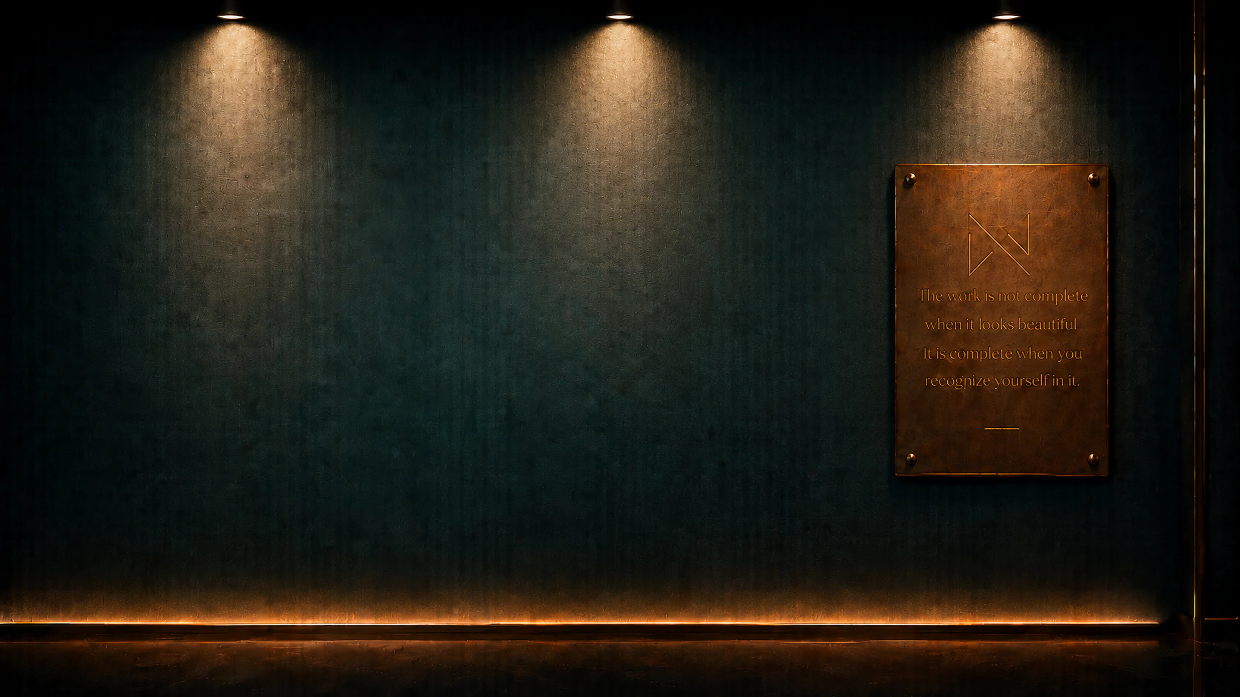 The gallery entrance: a dark teal wall washed by ceiling downlights above a lit baseboard.